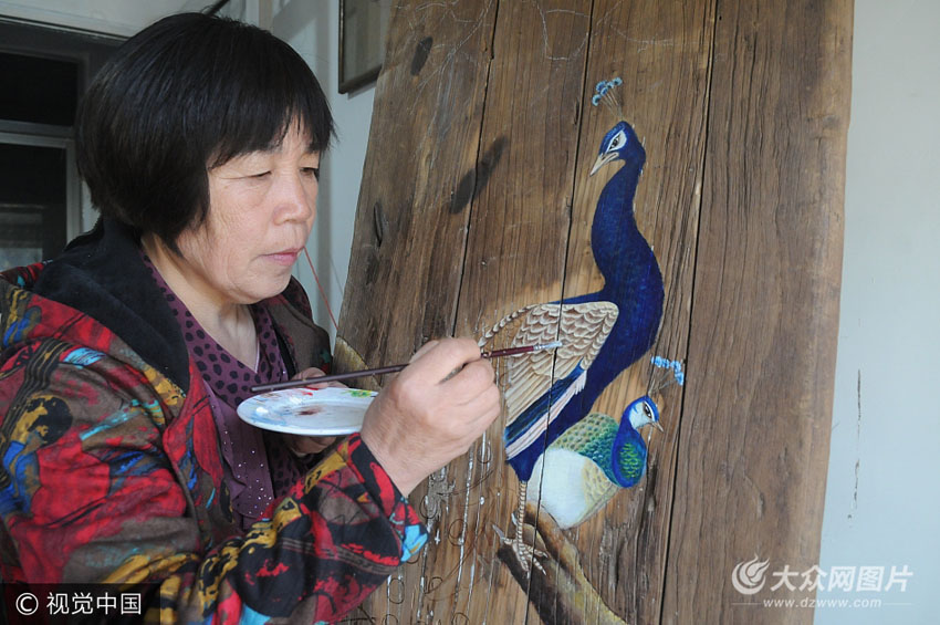 55岁的乡村女画家李玉莲正在旧门板上创作